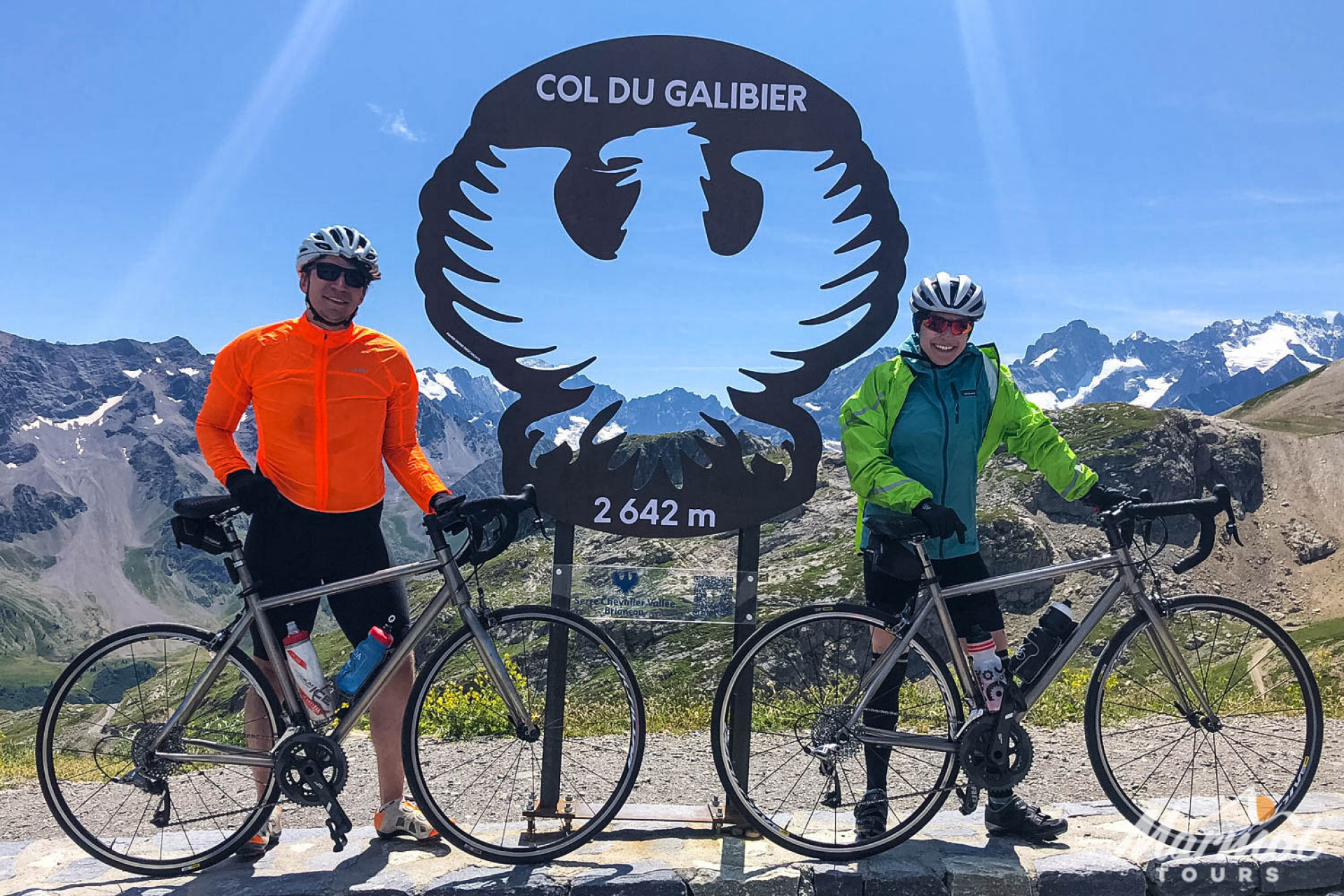 Pair of cyclist pose with Marmot Tours hire bike at Col du Galibier cycling climb summit