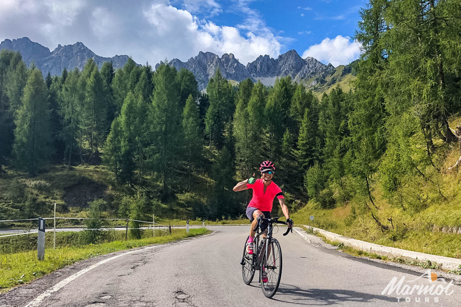 Female cyclist giving thumbs up on sunny ride with forest backdrop on Marmot Tours guided road cycling holiday in Europe