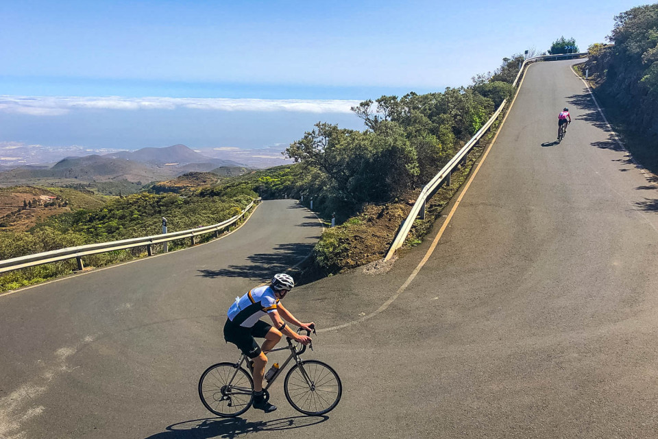 Pair of cyclists climbing with ocean in distance on guided road cycling tour Gran Canaria with Marmot Tours
