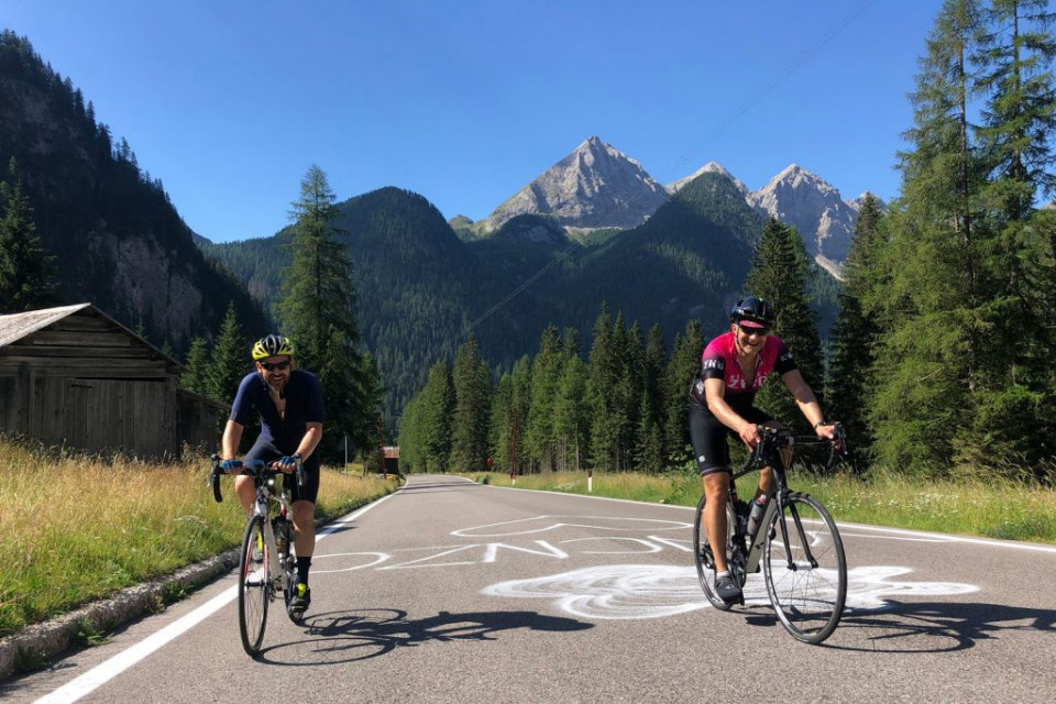 Pair of cyclists smiling with mountains backdrop cycling in the Dolomites with Marmot Tours guided road cycling holidays