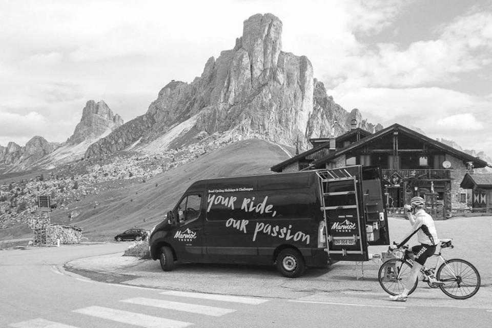 Black and white image of cyclist and Marmot Tours support vehicle at Passo Giau summit Dolomites Italy cycling holiday