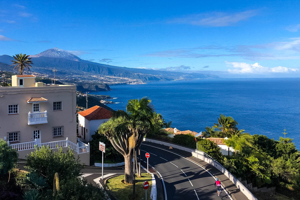 Bright blue skies above coastal road showing Atlantic Ocean, Mount Teide and cyclist on Marmot Tours Tenerife cycling holiday