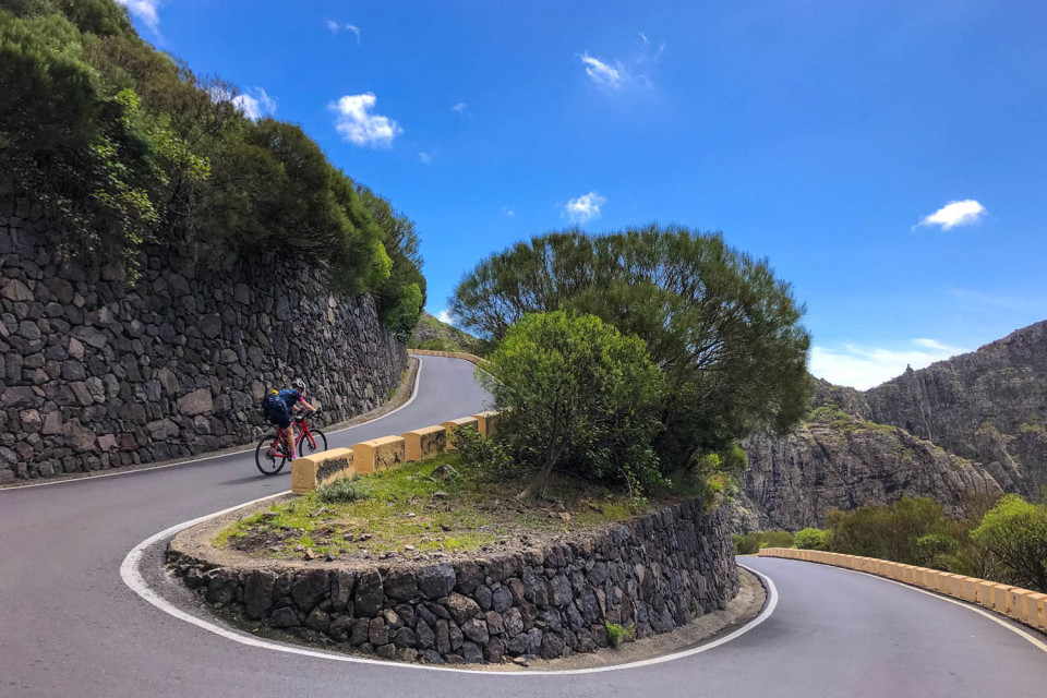 Female cyclist climbing steep climb with hairpin bend and forested slopes on Marmot Tours guided road cycling holiday Tenerife