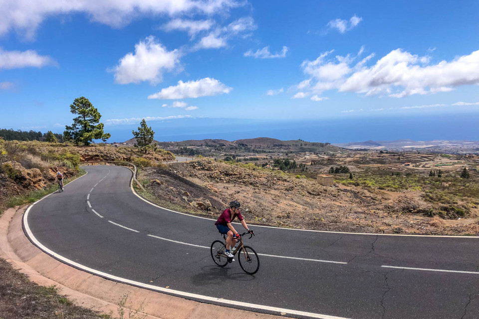 Cyclists climbing smooth road with sea background and blue sky with clouds on Marmot Tours guided road cycling tour Tenerife
